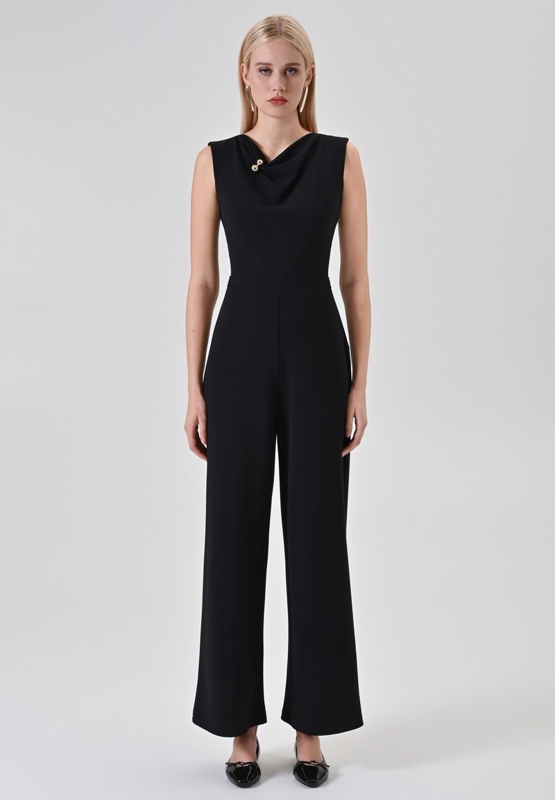 Combinaison noire avec col bénitier, détail accent doré, sans manches et pantalon à jambes larges, confectionnée dans un tissu lisse et extensible.