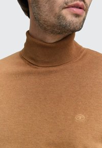 Maglione a collo alto marrone realizzato in un tessuto a maglia liscia, con un collarino aderente e un sottile logo sul petto.