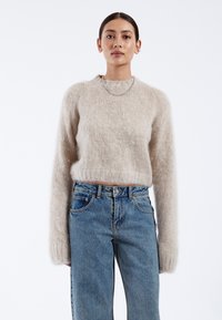 Light beige fuzzy sweater with a crew neck, voluminous sleeves, worn with high-waisted blue denim jeans. Simple silver chain necklace.