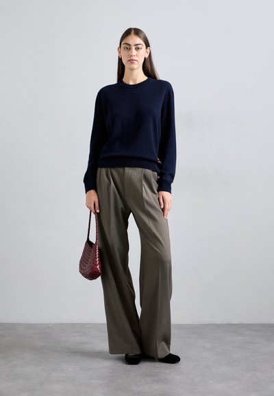 Navy knitted sweater, wide-leg gray trousers, black flats, and a burgundy woven handbag. Model stands against a light gray background.