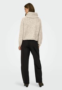 Maglione a coste grigio chiaro, cropped, con colletto alto e maniche lunghe, abbinato a pantaloni neri a gamba larga e calzature con tacco.