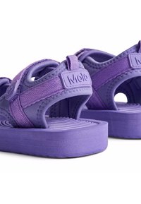 Violetit sandaalit, joissa on teksturoitu pohja, säädettävät hihnat ja pehmeä kumipohja. Brändin logo hihnassa. Kevyt malli.