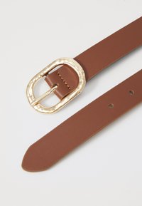 Bruine leren riem met een geslagen gouden gesp, voorzien van meerdere verstelgaten en een gladde textuur.