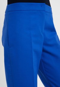 Niebieskie spodnie o gładkiej fakturze i dopasowanym kroju, z płaskimi kieszeniami z przodu i eleganckim fasonie bez widocznych zapięć.
