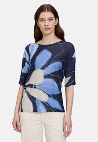 Granatowa bluzka w kwiaty z dużymi jasnoniebieskimi i kremowymi wzorami, krótki rękaw i okrągły dekolt, wykonana z lekkiego materiału.