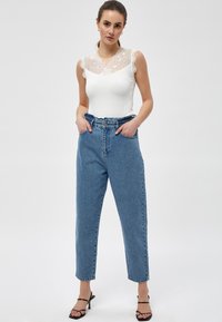 Body bianco con pizzo sul colletto abbinato a jeans in denim blu chiaro a vita alta, con una vestibilità rilassata e vita elastica.