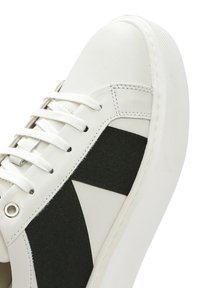 Baskets en cuir blanc avec un design épuré, détails en tissu noir, lacets plats et semelle en caoutchouc texturé pour une meilleure adhérence.