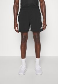 Svarta träningsshorts med elastisk midja, sidofickor med dragkedja och en subtil logotyp. Slät struktur och längd ovanför knäet.