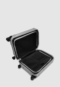 Maleta rígida gris con interior negro. Diseño abierto con compartimentos de malla, un bolsillo con cremallera y cuatro ruedas para facilitar su movilidad.