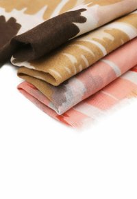 Quattro sciarpe piegate di colori marrone, beige e rosa con motivi astratti. Tessuto morbido con bordi frangiati e texture variabili.