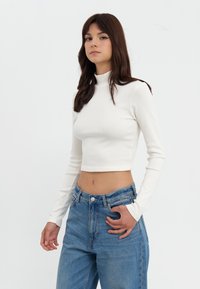 Hvit stripete langermet cropped topp med høy krage, parret med høyt liv blå denim jeans, med en avslappet passform og synlig søm.