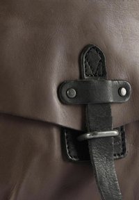 Braune Ledertasche mit strukturierter Oberfläche, ausgestattet mit einem schwarzen Lederriemen, der durch eine Metallschnalle und einen Druckknopfverschluss gesichert ist.