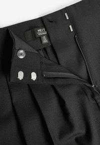 Pantalon noir à coupe droite avec une texture de tissu lisse, doté d'une fermeture à bouton et zip, et d'accents métalliques près de la ceinture.