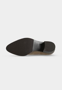 Semelle d'une chaussure de ville en cuir marron pointue montrant une semelle et un talon noirs texturés avec marquage de la marque et texte « Made in Portugal ».