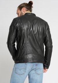 Sort læderjakke med quilted skulderdetaljer og lige pasform. Har en klassisk krave og diskrete spændeindlæg i taljen.