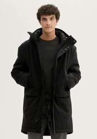 Musta polsterdatud parka kõrge kraega, esiküljel tõmblukk ja nupclosure'itega. Sellel on kaks suurt esiküljepocketit ja sile tekstuur.