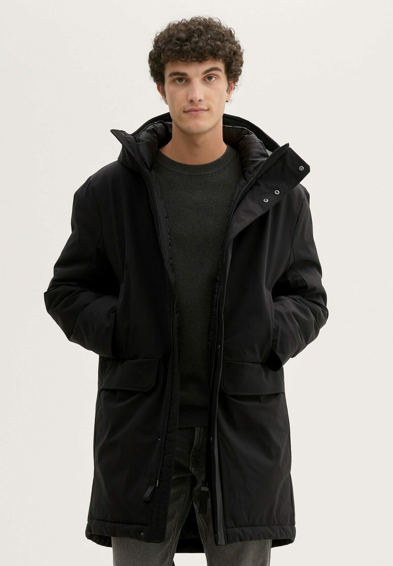 Musta polsterdatud parka kõrge kraega, esiküljel tõmblukk ja nupclosure'itega. Sellel on kaks suurt esiküljepocketit ja sile tekstuur.