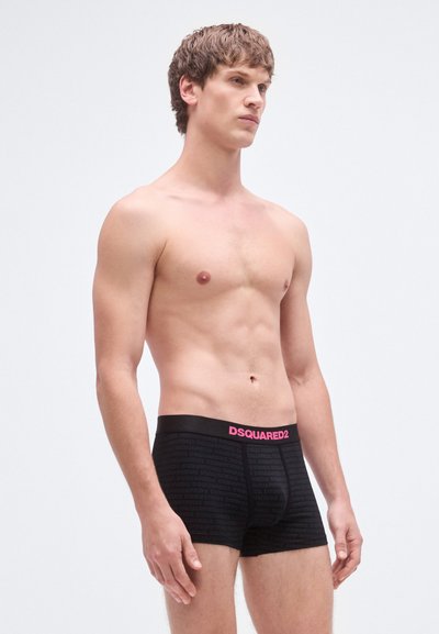 Fekete pamut boxernadrág texturált mintával; jellegzetes rózsaszín logós derékpánttal. A modell semleges környezetben.