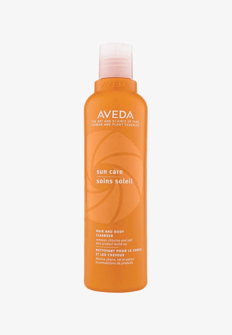 Botella de plástico naranja con tapa flip-top. Presenta texto blanco y un gráfico de sol, etiquetada como limpiador para cabello y cuerpo Aveda sun care.