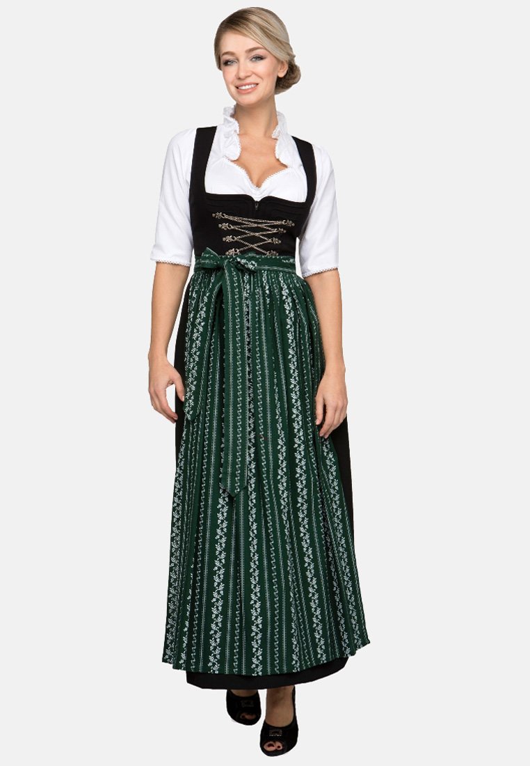 Traditionelles Dirndl, bestehend aus einem schwarzen Mieder mit silberner Schnürung und einem grünen Rock, der mit weißen Blumenmustern verziert ist. Begleitet von einer weißen Bluse.