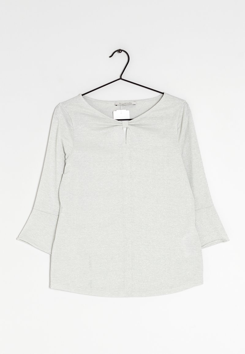 Jasnoszara bluzka z długim rękawem, dekoltem w kształcie litery V, delikatną teksturą, okrągłym dołem i małym węzełkiem na wysokości klatki piersiowej. Wisi na czarnym wieszaku.