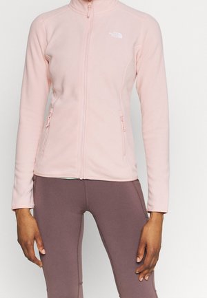 Osoba w pastelowo różowej polarowej bluzie na zamek błyskawiczny z logo The North Face i dopasowanych leginsach w kolorze mauve, stojąca na jednolitym tle.