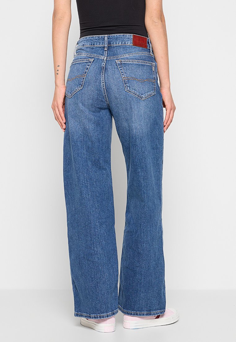 Weite blaue Denim-Jeans mit heller Waschung, fünf Taschen und einem Lederpatch am Bund. Genähte Details an den Gesäßtaschen.
