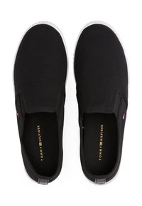 Sorte slip-ons laget av stoff med flat hvit gummisåle, med elastiske sideseksjoner og et logo på innersålen.