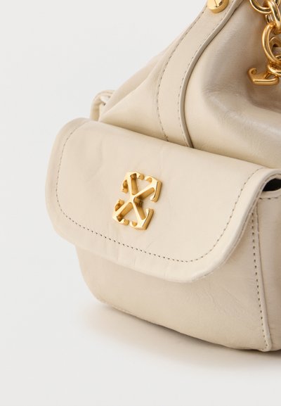 Μπεζ δερμάτινη τσάντα χειρός με μικρή μπροστινή τσέπη που διαθέτει χρυσό διασταυρωμένο λογότυπο βελών και χρυσή αλυσίδα για ιμάντα.