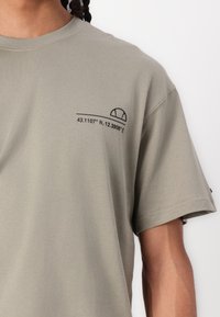 Camiseta de algodón color verde oliva con mangas cortas, cuello redondo y coordenadas impresas con un diseño de semi-círculo en el lado izquierdo del pecho.