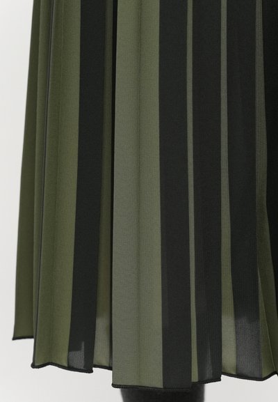 Pleated skirt in dark green and black fabric, featuring vertical stripes and a translucent texture. Hemline is finished with a simple stitch.