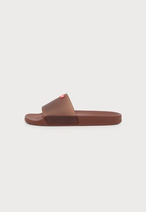 Braune Slip-On-Sandale mit breitem transparentem Riemen und kleinem roten Logo-Tag auf weißem Hintergrund.