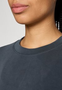 T-shirt blu scuro a girocollo con texture liscia, cuciture curate attorno al colletto e una vista ravvicinata della scollatura e della parte superiore del petto.