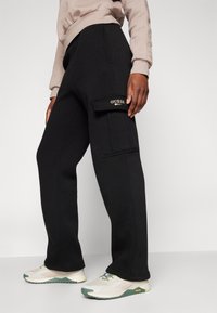 Svarta sweatpants med en avslappnad passform, utrustade med en sidficka och en gyllene "GUESS"-logotyp. Slätt tyg med en klassisk design.