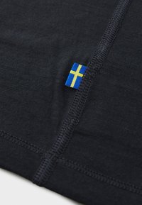 Svart tekstil med en synlig blå og gul svensk flagg etikett, med en glatt tekstur og kontrasterende søm langs kantene.