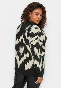 Maglione a fantasia nero e crema con vestibilità ampia, caratterizzato da un design geometrico e una texture a coste. Maniche lunghe e collo a giro.