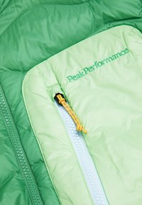 Grüne Pufferjacke mit glänzendem Finish; verfügt über eine Reißverschlusstasche mit gelbem Kordelzug und gesticktem Logo in dunklerem Grün auf dem Stoff.