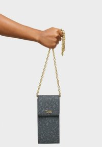 Bolso cruzado de cuero gris con una correa de cadena dorada, que cuenta con un patrón texturizado y cierre de solapa. Logo exhibido de manera destacada en la parte frontal.