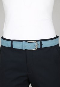 Helle blaue Wildledergürt mit silberner Schnalle, über schwarzen Hosen und einem weißen Oberteil getragen, zentriert auf der Taille.