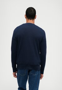 Granatowy sweter z długim rękawem i okrągłym dekoltem, o teksturowanej tkaninie, z prążkowanymi mankietami i dołem, zestawiony z dżinsami.