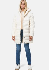 Witte pufferjas met horizontale stiksels, een capuchon en drukknoopsluiting. Draag het over een beige sweater en spijkerbroeken, met witte sneakers.