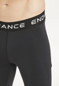 Svarta träningsleggings gjorda av elastiskt tyg, med en bred svart midja med vit text "ENDURANCE" och en slät yta.