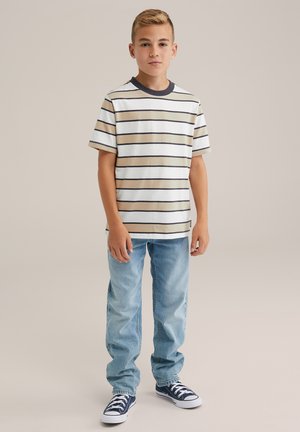 Gestreept T-shirt met korte mouwen in crème, bruin en marineblauw, gecombineerd met lichtblauwe denim spijkerbroek en blauwe sneakers, staand op een neutrale achtergrond.