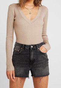 Beige geribbelde longsleeve bodysuit met een diepe V-hals, gecombineerd met hoge zwarte denim shorts met franjekanten en koperen knoop accenten.