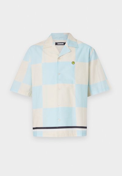 Camisa de botones de manga corta en un patrón a cuadros en azul claro y crema, con un parche de sonrisa verde y una franja oscura en el dobladillo.