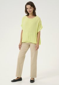 Top corto de gran tamaño en un brillante color amarillo, de manga corta y con tela texturizada, combinado con pantalones rectos de un ligero color beige y flats negros.