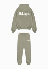 Set van olijfgroene hoodie en joggingbroek gemaakt van zachte stof. Voorzien van witte logotekst op de achterkant en voorkant van de broek. Relaxte pasvorm.