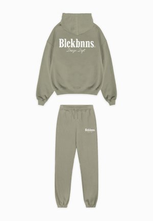 Set van olijfgroene hoodie en joggingbroek gemaakt van zachte stof. Voorzien van witte logotekst op de achterkant en voorkant van de broek. Relaxte pasvorm.