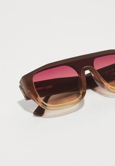 Silmät, joissa on ruskea ja amber-väri, ja ne on muotoiltu näyttävästi geometrisesti. Vaaleanpunaiset linssit ja "CHERRY LASRY" -brändäys sisävarressa.