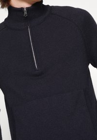 Marinblå halvmång vid sweater gjord av texturerad stickad tyg, med en ribbad krage och en subtil framficka. Minimalistisk design med strömlinjeformat utseende.